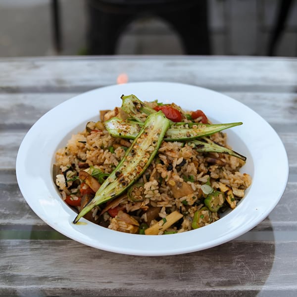 Cajun jambalaya with rice, vegetables, and grilled okra in a white bowl on a wooden table.