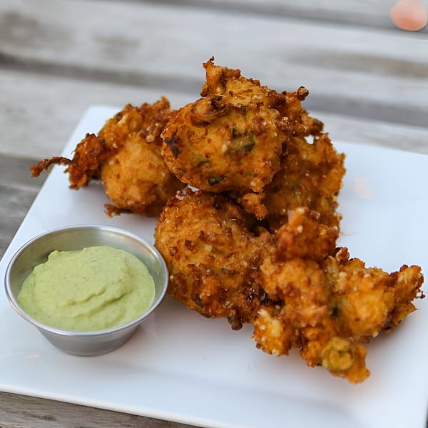 Golden-brown Cajun hushpuppies with a side of green dipping sauce on a white plate.