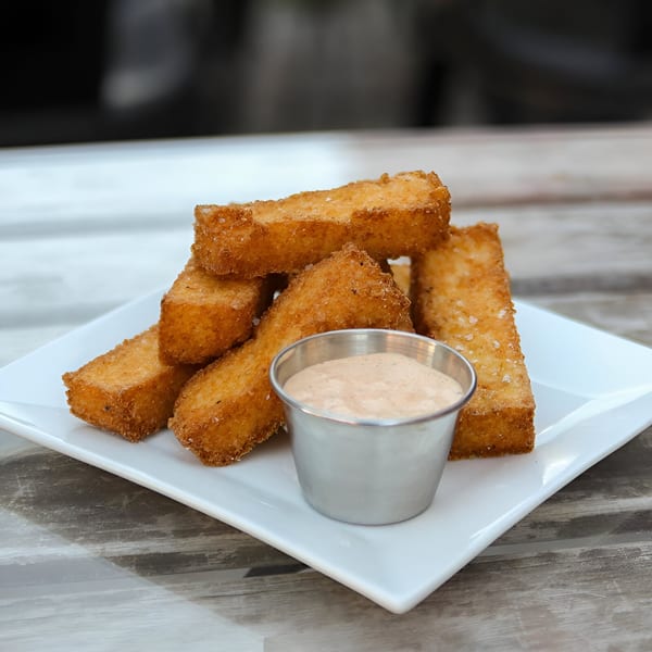 Golden brown fried grit fries with a side of creamy dipping sauce on a white plate.