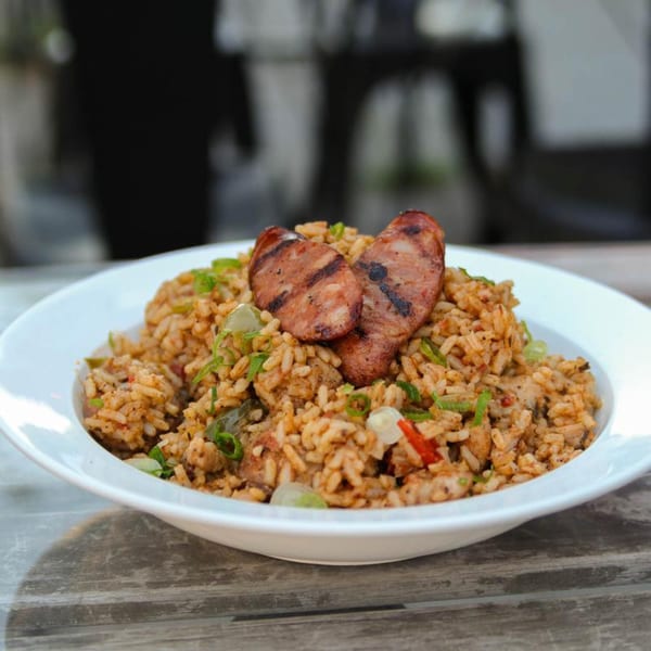 Cajun jambalaya with grilled sausage slices and green onions in a white bowl on a wooden table.
