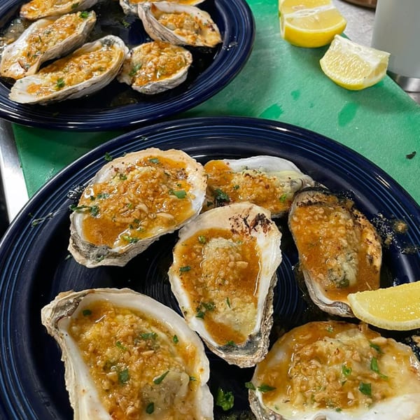 Two blue plates filled with baked oysters, garlic topping, parsley, and lemon wedges.