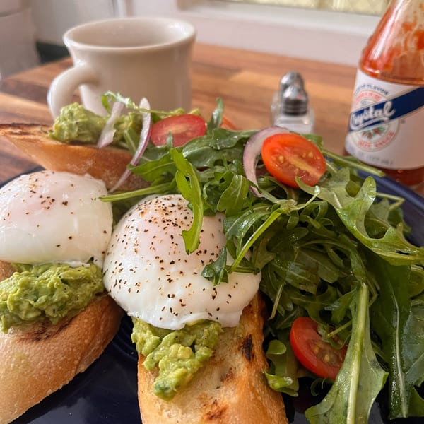 Avocado toast with poached eggs, a fresh arugula salad, and hot sauce on a blue plate.