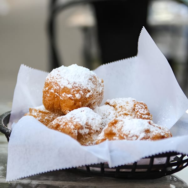 A basket of Krewe of McGinley Square's cajun beignets, generously dusted with powdered sugar.
