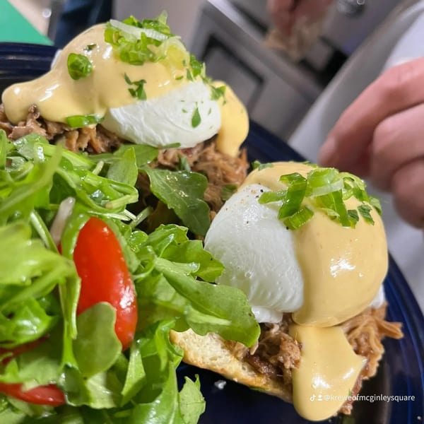 Two pulled pork eggs benedict with hollandaise, green onions, and a fresh arugula salad.