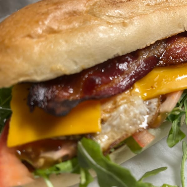 Sandwich with glazed bacon, melted cheese, fried egg, tomato, and fresh arugula.