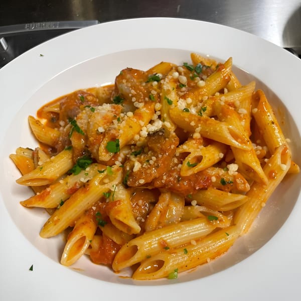 Cajun penne pasta with shrimp, red sauce, parmesan cheese, and parsley in a white bowl.